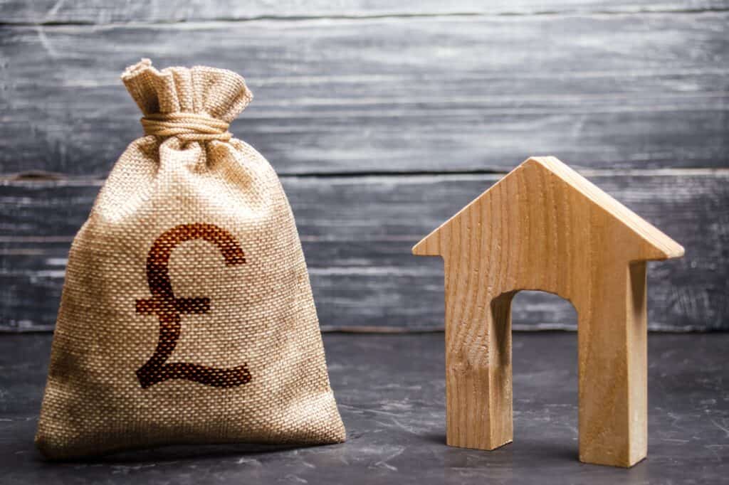 A money bag with a British pound sign and a wooden house figurine in the concept of 'Lewisham Removals Cost'.