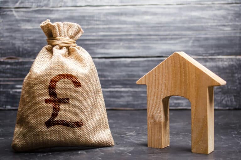 A money bag with a British pound sign and a wooden house figurine in the concept of 'Lewisham Removals Cost'.