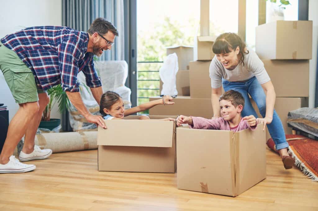 A happy family playing with carton after moving in the concept of 'What to Do With Packing Materials After Moving House'.